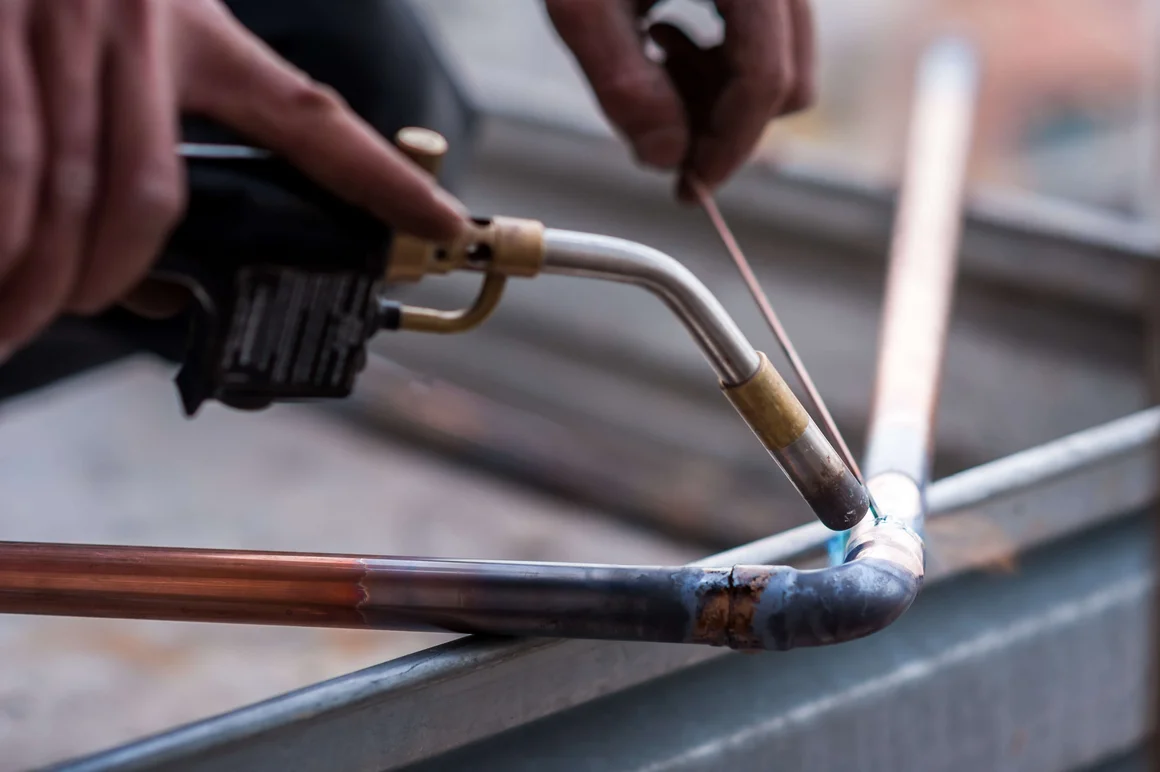 Person lötet Kupferrohre mit Gasbrenner.